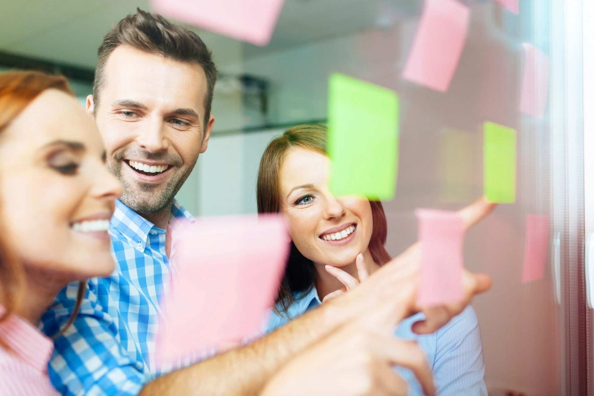 A man and woman pointing at post it notes on the wall.