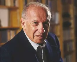 A man in suit and tie standing next to books.